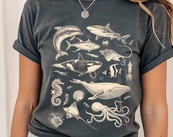 May include: Dark gray t-shirt featuring a detailed illustration of various marine animals, including a dolphin, shark, orca, seahorse, whale, and octopus. The design is in a vintage style, with a faded, slightly distressed appearance.