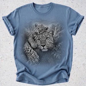 May include: A dusty blue crew neck t-shirt featuring a detailed black and white graphic print of a leopard resting on a tree branch with a cub perched on its head, surrounded by a jungle scene with ferns and a distant waterfall.