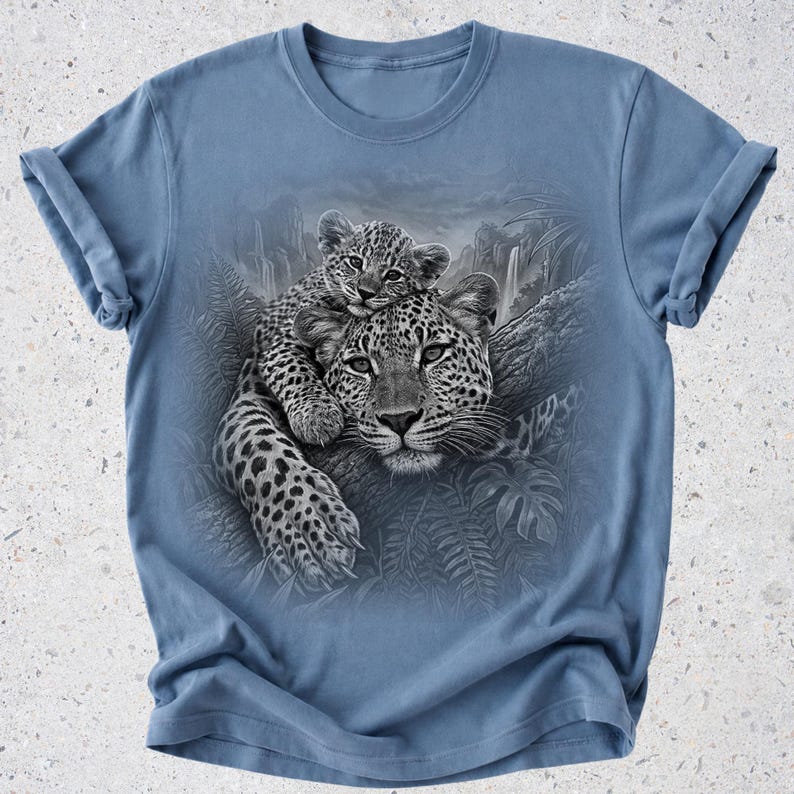 May include: A dusty blue crew neck t-shirt featuring a detailed black and white graphic print of a leopard resting on a tree branch with a cub perched on its head, surrounded by a jungle scene with ferns and a distant waterfall.