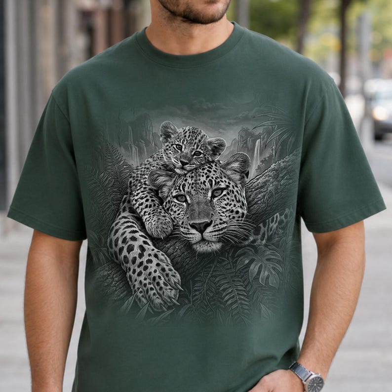 May include: A dark green short-sleeve t-shirt featuring a detailed monochromatic graphic print of a leopard resting on a tree branch with a cub perched on its back, set against a backdrop of lush jungle foliage and a waterfall.