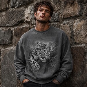 May include: A charcoal gray crewneck sweatshirt featuring a detailed black and white graphic print of an adult leopard with a cub resting on its back, set against a backdrop of jungle foliage and a waterfall.