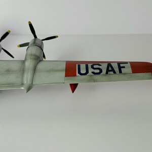 Pu&ograve; includere: Un modello dettagliato di aereo con ali argentate e coda con punta rossa. Il modello presenta quattro eliche con pale nere e punte gialle. Il testo "USAF" &egrave; stampato sull'ala.