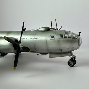 Pu&ograve; includere: Modello dettagliato di un bombardiere d'argento della United States Air Force. Il modello presenta quattro eliche nere con punte gialle, un abitacolo trasparente e la scritta "UNITED STATES AIR FORCE" sul lato. Il carrello di atterraggio &egrave; visibile.