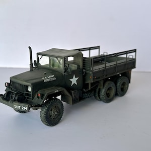 Può includere: Modello dettagliato di un camion dell'esercito americano, verniciato in verde oliva. Il camion presenta un cassone, una cabina con tetto in tela e una stella bianca. Il testo "U.S. ARMY 05852169" e "523T 214" è visibile.