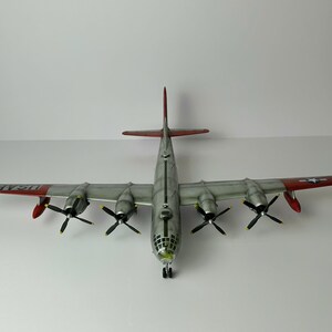 Pu&ograve; includere: Modello dettagliato di un aereo B-29 Superfortress, visto dall'alto. L'aereo ha quattro eliche, ali argentate con estremit&agrave; rosse e la scritta "USAF" sulle ali. Il modello &egrave; posto su uno sfondo bianco.