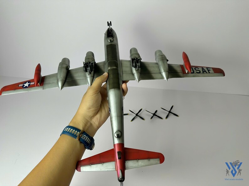 Pu&ograve; includere: Modello dettagliato di aereo con fusoliera argentata ed estremit&agrave; alari rosse. Le ali mostrano il testo "USAF" e un'emblema a stella. Quattro eliche nere sono posizionate vicino all'aereo.