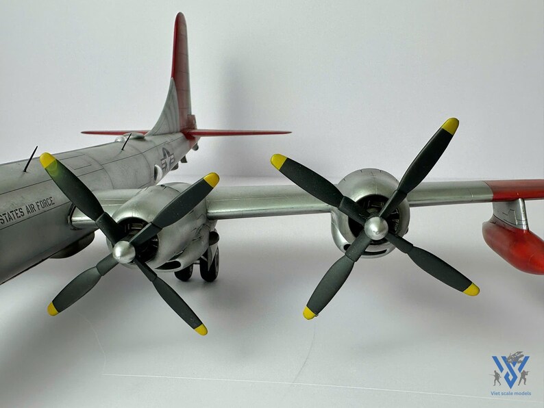 Pu&ograve; includere: Un modello dettagliato di un aereo argento e grigio con quattro eliche nere con punte gialle. La pinna di coda &egrave; rossa e grigia. Le parole "UNITED STATES AIR FORCE" sono visibili sul lato dell'aereo.