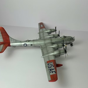 Pu&ograve; includere: Modello dettagliato di un bombardiere B-29 Superfortress argento e rosso. Il modello presenta quattro eliche, la scritta "UNITED STATES AIR FORCE" e le lettere "USAF" sulla coda. Le ali e la coda hanno accenti rossi.