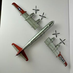 Pu&ograve; includere: Modello dettagliato di aereo con fusoliera argentata e ali grigie, con accenti rossi sulla coda e sulle estremit&agrave; alari. Il modello include quattro eliche nere e marcature, tra cui "USAF" e un'insegna a stella. Modello B-29 Superfortress.