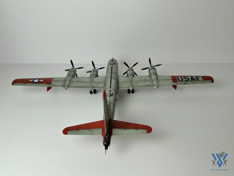 Pu&ograve; includere: Un modello dettagliato di aereo, con una combinazione di colori argento e rosso e quattro eliche. Le ali mostrano il testo "USAF" e un'emblema a stella. Il modello &egrave; una replica di un aereo d'epoca.