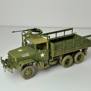 Può includere: Modello verde oliva di un camion dell'esercito americano, con mitragliatrice montata, insegne a stella bianca e la scritta "U.S. ARMY 05852169". Il camion ha sei ruote e un cassone.
