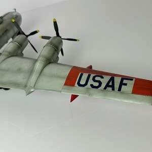Pu&ograve; includere: Un modello dettagliato di aereo con corpo grigio, eliche nere e accenti alari rossi e bianchi. L'ala mostra il testo "USAF" in blu. Il modello &egrave; una rappresentazione di un aereo d'epoca.