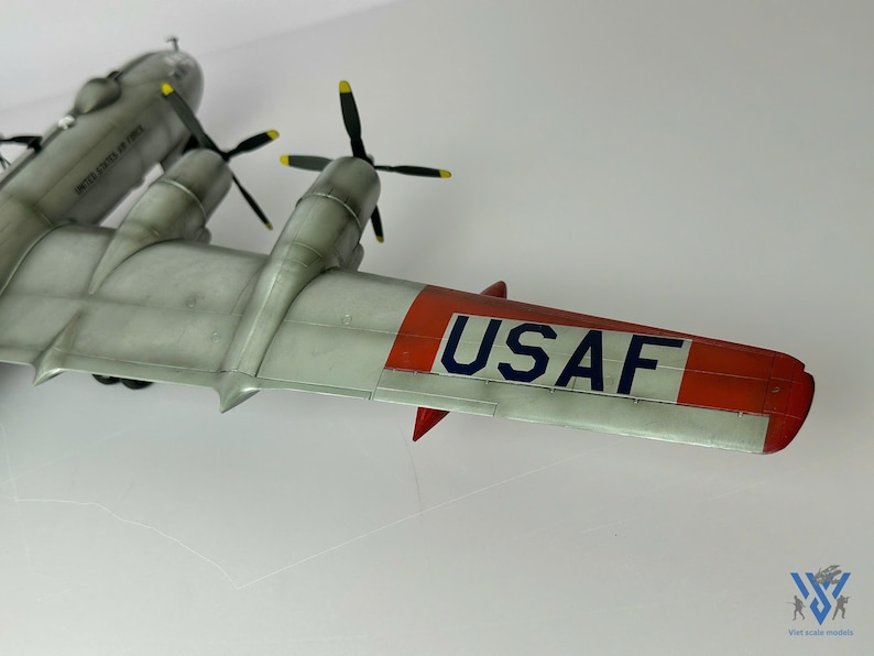 Pu&ograve; includere: Un modello dettagliato di aereo con corpo grigio, eliche nere e accenti alari rossi e bianchi. L'ala mostra il testo "USAF" in blu. Il modello &egrave; una rappresentazione di un aereo d'epoca.