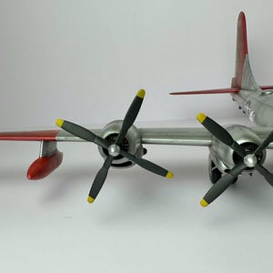 Pu&ograve; includere: Modello dettagliato di aereo con fusoliera argentata, dettagli rossi e gialli sulle ali e sulla coda, e quattro eliche nere con punte gialle. Il modello ha un design dettagliato ed &egrave; ambientato su sfondo bianco.