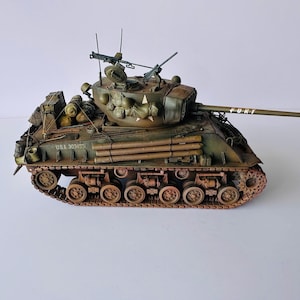 May include: A detailed model of a military tank, painted in olive green and brown tones. The tank features a long gun barrel, a rotating turret, and various accessories. The word "FURY" is written on the barrel. The model includes the text "U.S.A. 303435".