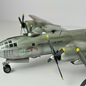 Pu&ograve; includere: Modello dettagliato di un bombardiere d'argento dell'aeronautica militare statunitense. Il modello presenta quattro eliche con punte gialle, un abitacolo dettagliato e la scritta "Caribbean Queen" con un'illustrazione.