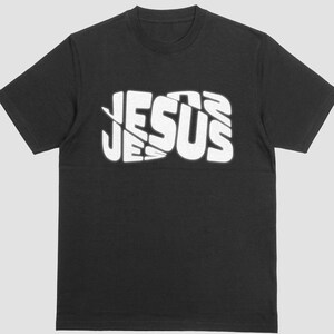 May include: Black t-shirt with the word "JESUS" in large, white, stylized lettering across the chest. The text has a layered, slightly distorted appearance. The shirt has short sleeves and a crew neck.
