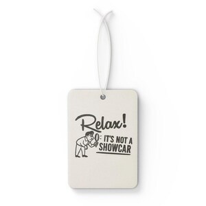 May include: Cream-coloured rectangular air freshener with a white string. The air freshener features the words "Relax! It's not a showcar" in black, alongside a cartoon illustration of a man.