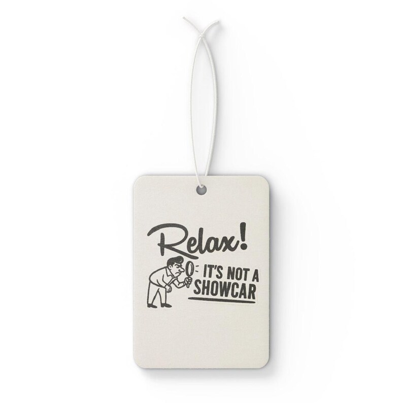 May include: Cream-coloured rectangular air freshener with a white string. The air freshener features the words "Relax! It's not a showcar" in black, alongside a cartoon illustration of a man.