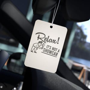 May include: An off-white rectangular car air freshener with the text "Relax! It's Not a Showcar" in black. The air freshener is suspended by a string, featuring a cartoon illustration of a person inspecting a car.