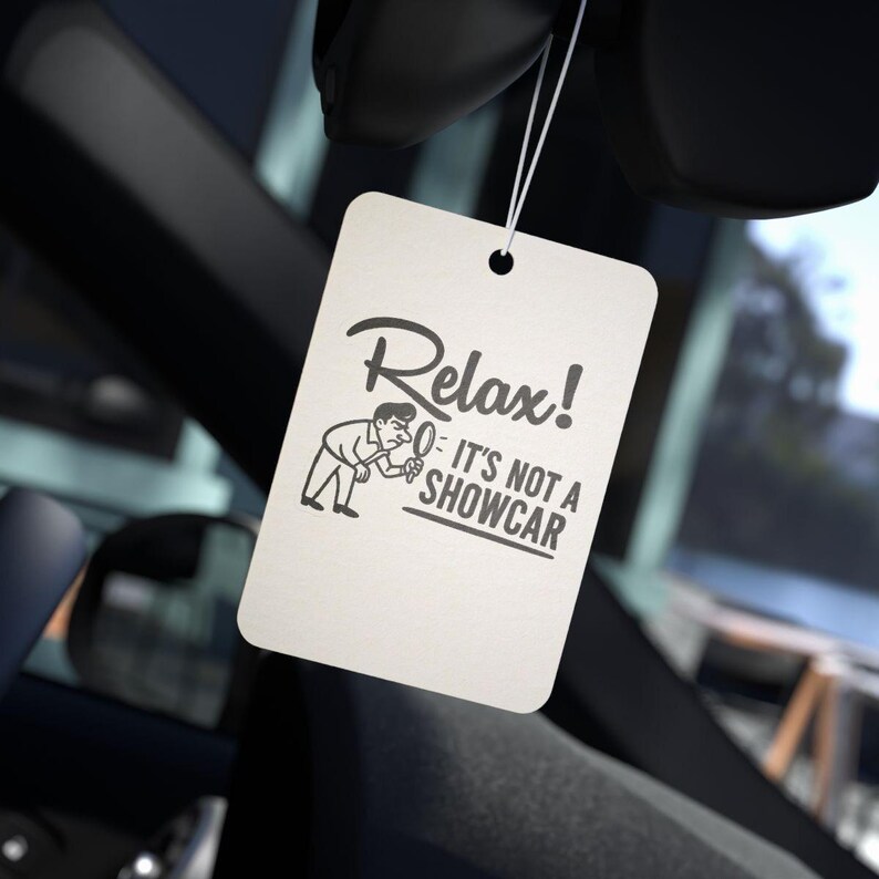 May include: An off-white rectangular car air freshener with the text "Relax! It's Not a Showcar" in black. The air freshener is suspended by a string, featuring a cartoon illustration of a person inspecting a car.