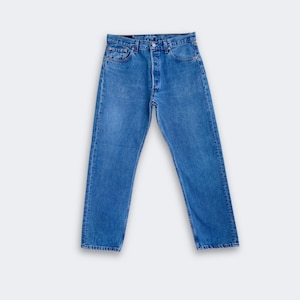 May include: A pair of medium-wash blue denim jeans featuring a classic five-pocket design, a button fly closure, and a straight-leg cut. The jeans have a standard waistband with belt loops and copper-toned metal rivets at the pocket corners.