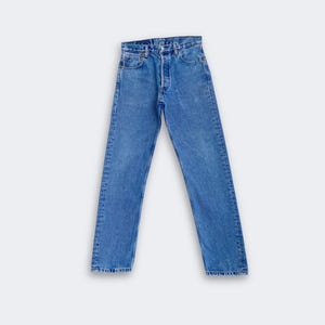 Könnte beinhalten: Eine mittelblaue Jeans aus Denim mit hoher Taille, klassischem Fünf-Taschen-Design, Knopfleiste und geradem Beinverlauf. Der Stoff hat einen gleichmäßigen Blauton mit dezenten Aufhellungen an den Oberschenkeln und den Nähten.