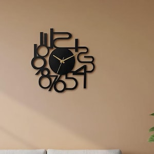 May include: Black, modern wall clock with a unique, abstract design. The clock features a circular face with gold hands and stylized black numerals. The clock is mounted on a beige wall, above a light gray sofa.