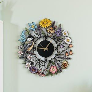 Può includere: Un orologio da parete decorativo con un quadrante nero e lancette e numeri dorati. L'orologio è circondato da una ghirlanda di fiori colorati e un uccello dettagliato. L'orologio è montato su una parete verde chiaro.