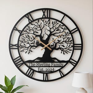 Può includere: Orologio da parete in metallo nero con un design ad albero della vita. L'orologio presenta numeri romani, lancette in legno e la scritta "The Sterling Family Est. 2024". Il design dell'albero include un gufo, un cervo e un uccello.