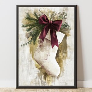 May include: Framed artwork featuring a Christmas stocking with a burgundy bow and evergreen sprigs. The stocking is off-white with a textured appearance, set against a backdrop of gold and white brushstrokes. The frame is black.