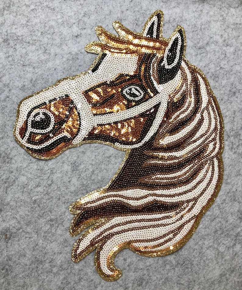 May include: A horse head applique with a gold sequin outline. The horse is made of white, brown, and gold sequins. The horse's mane and face are detailed with various sequin colors and patterns. The applique is on a gray background.