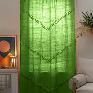 May include: Bright green curtain with a textured appearance. The curtain has a scalloped top and is adorned with rows of decorative tassels. The curtain is hanging in front of a window, and the light filters through the fabric.