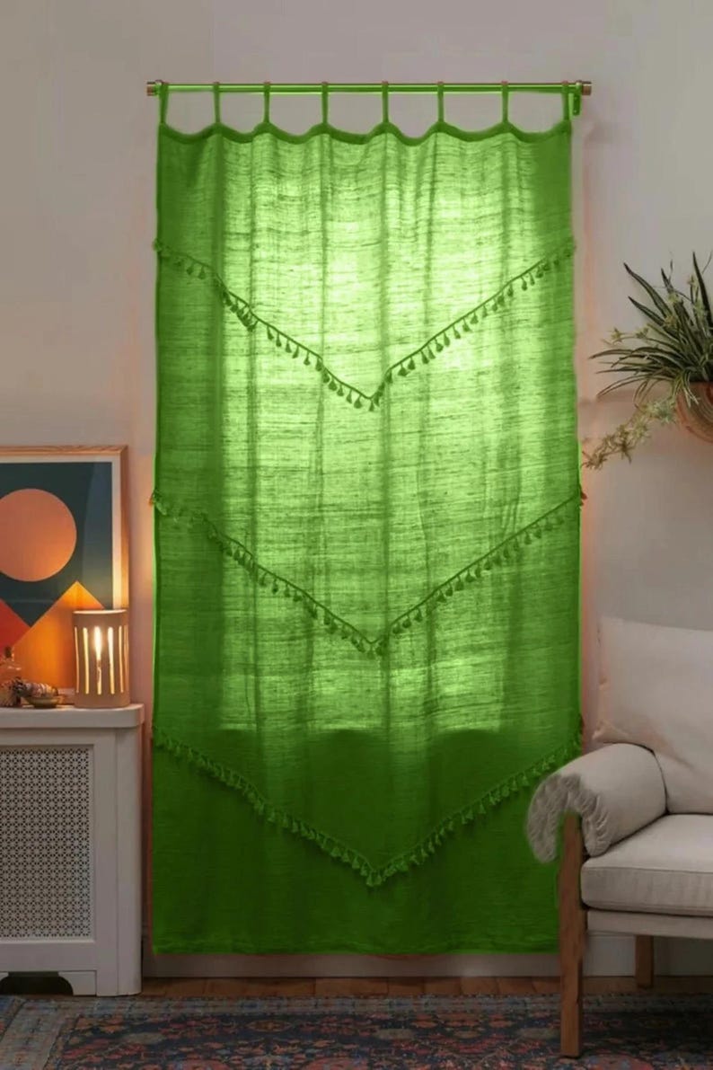 May include: Bright green curtain with a textured appearance. The curtain has a scalloped top and is adorned with rows of decorative tassels. The curtain is hanging in front of a window, and the light filters through the fabric.