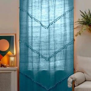 May include: Teal-colored curtain with a scalloped top and decorative tassel trim. The curtain hangs from a wooden rod and features a geometric design. The curtain is made of a textured fabric and adds a touch of bohemian style to a room.