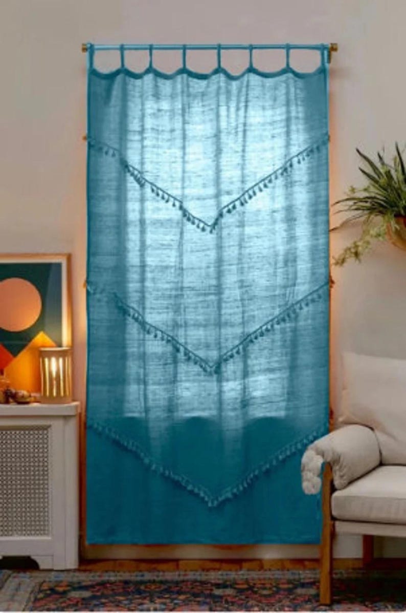 May include: Teal-colored curtain with a scalloped top and decorative tassel trim. The curtain hangs from a wooden rod and features a geometric design. The curtain is made of a textured fabric and adds a touch of bohemian style to a room.