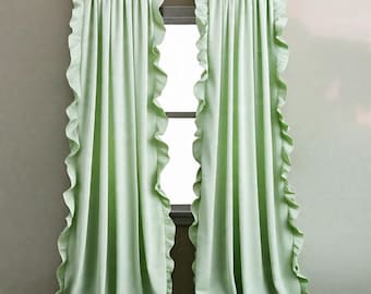 May include: Two light green ruffled curtains hanging on a decorative rod. The curtains are made of a soft fabric and have a ruffled edge. The curtains are hanging in front of a window.
