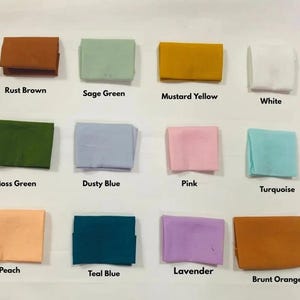May include: A collection of folded fabric squares in various colors, including rust brown, sage green, mustard yellow, and white. Additional colors are moss green, dusty blue, pink, turquoise, peach, teal blue, lavender, and burnt orange. Each square has a color label.