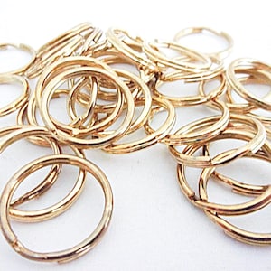 May include: A collection of gold-colored key rings, scattered on a white surface. The key rings are circular, with a split in the ring for attaching keys. The rings are made of metal and have a shiny finish.