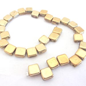 May include: A strand of gold-colored square beads, some of which are strung together in a circle, while others are strung in a straight line.