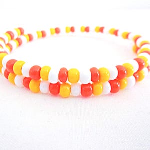 May include: A beaded bracelet with a spiral design. The bracelet features a repeating pattern of white, yellow, and orange beads. The beads are small and round, creating a colorful accessory.
