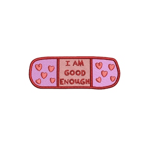 Può includere: Toppa ricamata a forma di cerotto. La toppa è principalmente rosa e rossa, con le parole "I AM GOOD ENOUGH" ricamate al centro. Piccoli cuori rossi sono ricamati su entrambi i lati del testo.