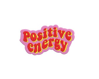 May include: A pink embroidered patch with the words "Positive Energy" in red, outlined in yellow. The text has a retro, bubble-letter style. The patch has a wavy, cloud-like shape.