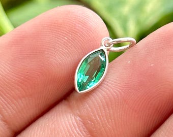 Peut inclure: Un petit pendentif en pierre précieuse verte de taille marquise serti dans une monture en métal argenté. Le pendentif présente une surface à facettes qui reflète la lumière et comprend un petit anneau circulaire au sommet pour le fixer.