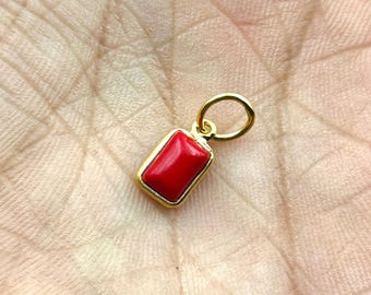 Peut inclure: Un pendentif rectangulaire en pierre précieuse rouge avec un cadre doré et une petite boucle en haut. Le pendentif est d'un rouge vif et semble être fait d'une pierre polie. Le cadre doré ajoute une touche d'élégance au bijou.