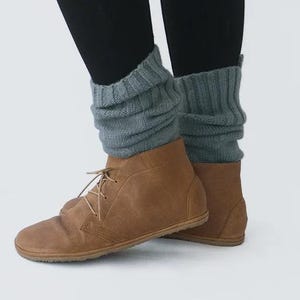May include: A pair of brown leather ankle boots with laces. The boots are worn with gray knitted leg warmers.