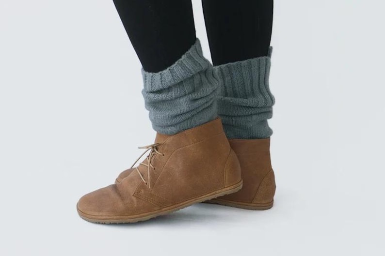 May include: A pair of brown leather ankle boots with laces. The boots are worn with gray knitted leg warmers.