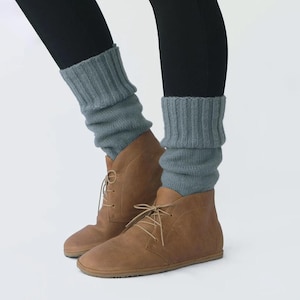 May include: A pair of brown leather ankle boots with laces. The boots are worn with gray knitted leg warmers.