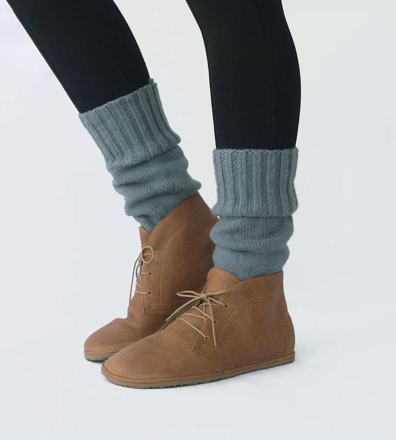 May include: A pair of brown leather ankle boots with laces. The boots are worn with gray knitted leg warmers.