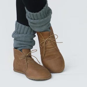 May include: A pair of brown leather ankle boots with laces. The boots are worn with gray knitted leg warmers.